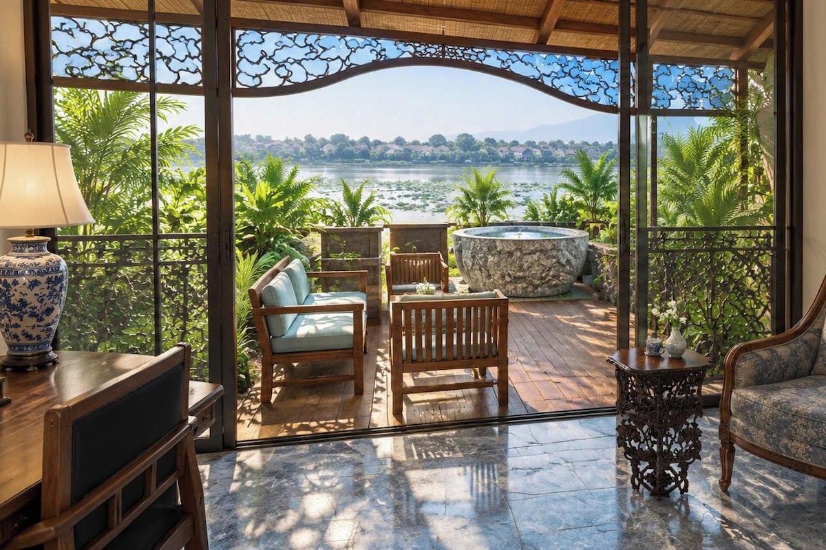 A balcony with a view of a lake, wooden furniture, and a decorative vase.