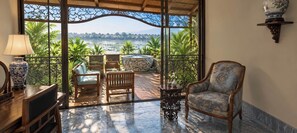 A balcony with a view of a lake, wooden furniture, and a decorative vase. - Thiên Ý Lake Hotel (Phu Xuan)
