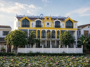A two-story building with a yellow facade, large windows, and a decorative roof. - Thiên Ý Lake Hotel (Phu Xuan)
