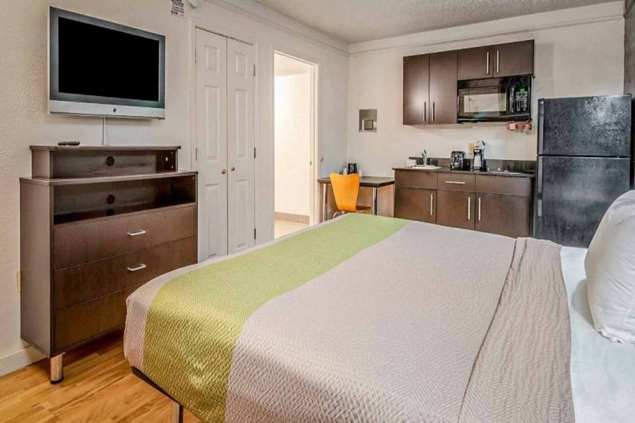 Een hotelkamer met een bed, een televisietoestel, een kitchenette en een deur die naar een andere kamer leidt.
