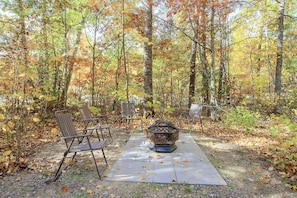 An outdoor seating area with metal chairs and a fire pit in a forested setting. - Near Kitchi Lake! Northwoods Retreat w/ Fire Pit (Blackduck)