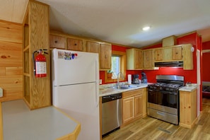 A compact kitchen with wooden cabinets, a stainless steel refrigerator, a dishwasher, a stove, and a window with a view. - Near Kitchi Lake! Northwoods Retreat w/ Fire Pit (Blackduck)