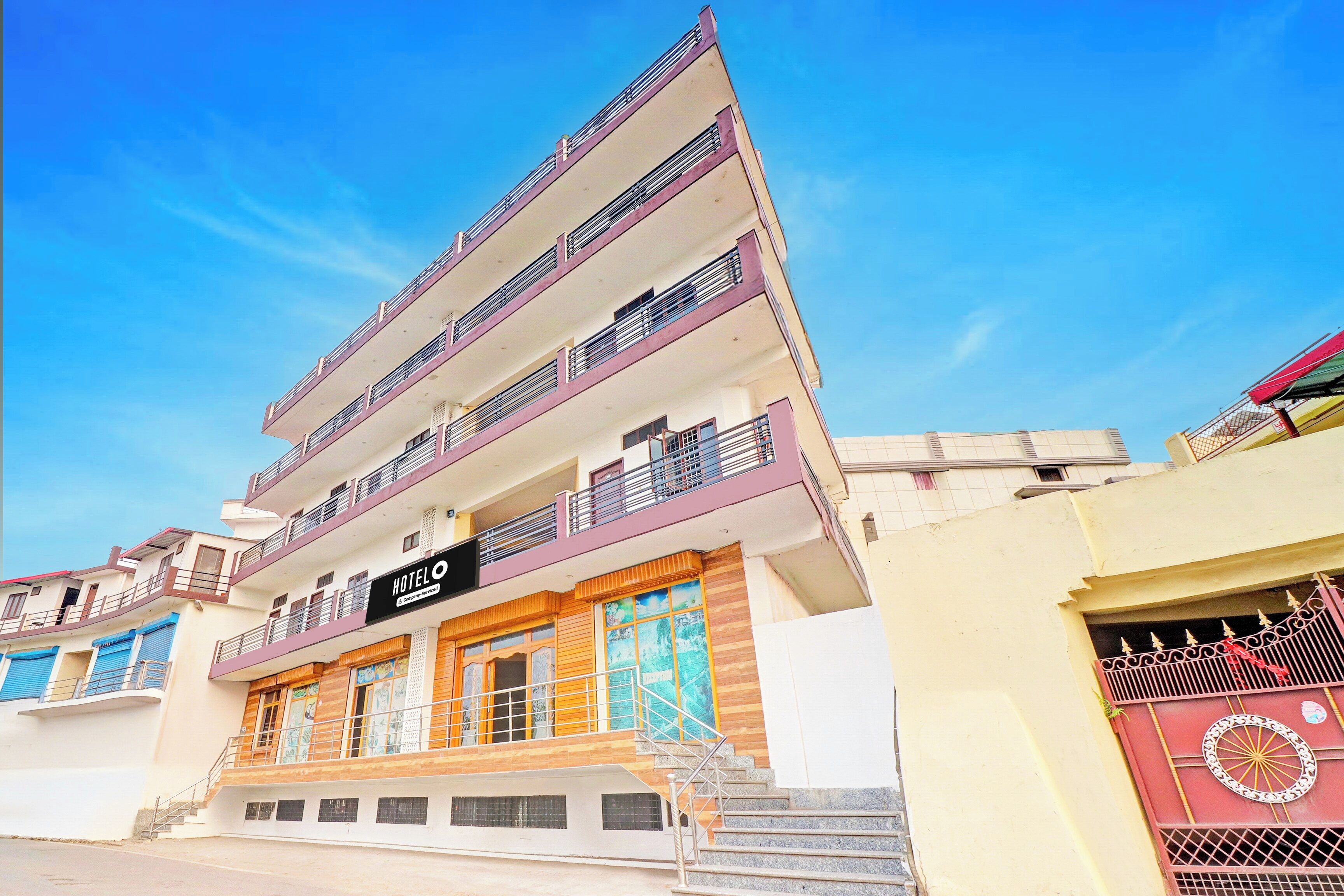 A multi-story hotel with balconies, a sign indicating it's a company-serviced hotel, and a staircase leading to the entrance.