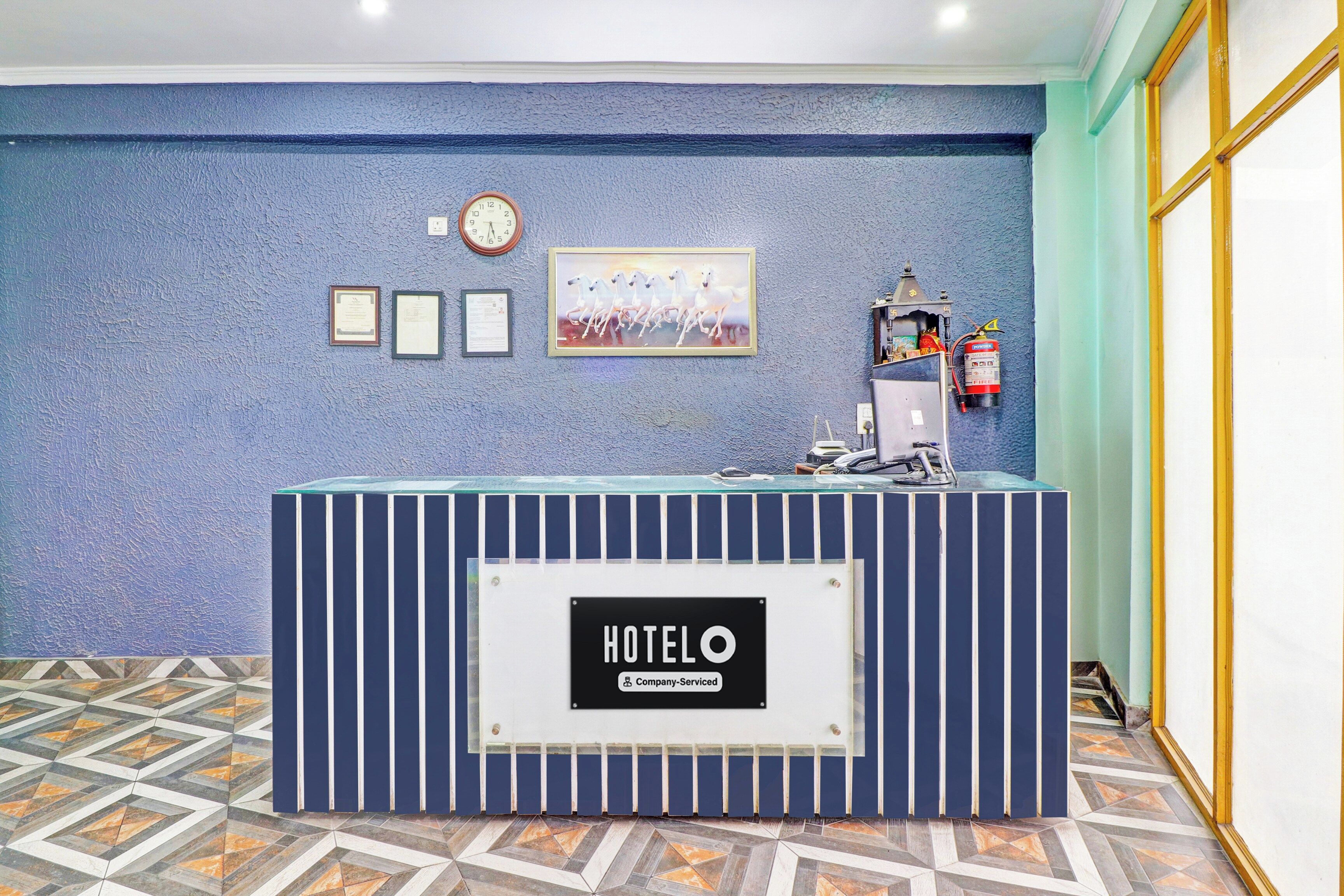A hotel reception desk with a clock, framed certificates, and a fire extinguisher.