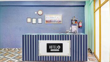 A hotel reception desk with a clock, framed certificates, and a fire extinguisher.