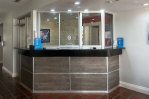 A reception desk with a glass enclosure, a stone wall in the background, and a tiled floor. - 1 King Bed | Non-Smoking (Dallas)