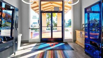 A hotel entrance with a modern design, including a reception desk, a digital screen, and a colorful mat with the hotel logo.