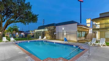 A swimming pool with lounge chairs and a building with a sign in the background.