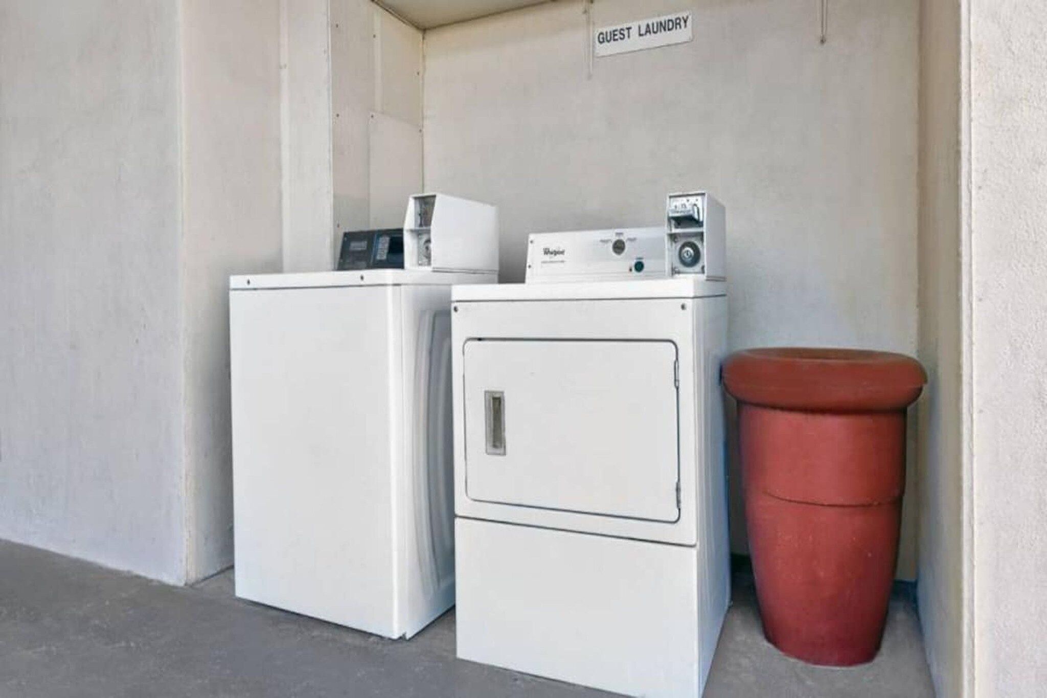 A laundry area with two white washing machines and a red trash bin.