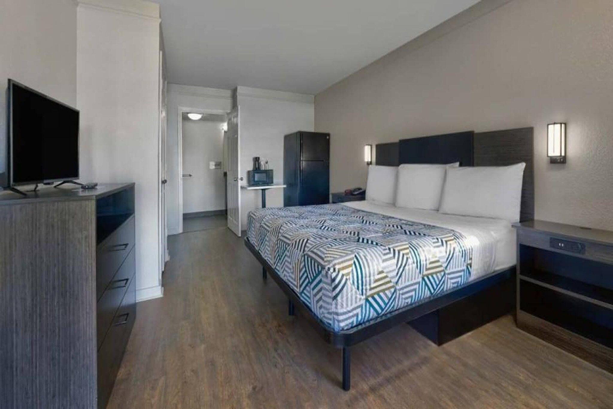 A hotel room with a bed, bedside tables, a television, a wardrobe, and a bathroom visible through an open door.