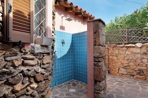 A stone-walled bathroom with a blue-tiled shower area and a wooden door. - Villa 'Nica' with Private Terrace and Private Garden (Golfo Aranci)