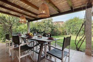 An outdoor patio with a table set for dining, surrounded by chairs, under a thatched roof. - Villa 'Nica' with Private Terrace and Private Garden (Golfo Aranci)