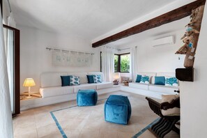 A living room with a white sofa, blue cushions, a blue ottoman, and a wooden coffee table. - Villa 'Nica' with Private Terrace and Private Garden (Golfo Aranci)