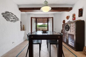 Un coin repas avec une table en bois, des chaises et une vue sur un jardin, accessible par une porte ouverte.