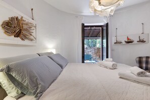 A bedroom with a bed, pillows, a view of the outdoors, and a stone wall. - Villa 'Nica' with Private Terrace and Private Garden (Golfo Aranci)