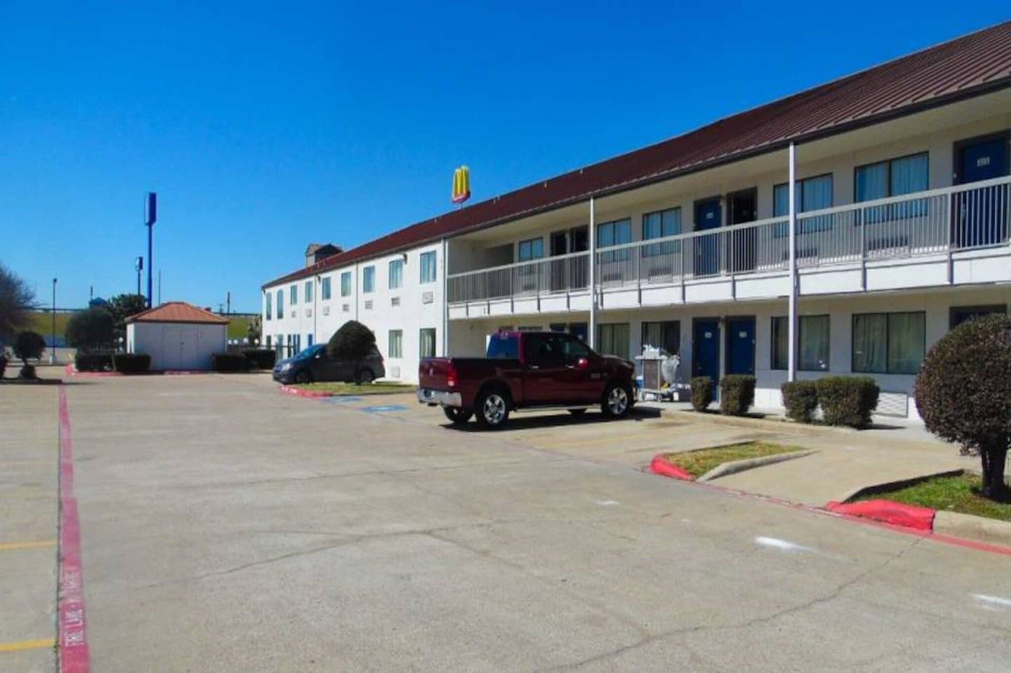 A motel with a two-story building, a parking lot, and a red pickup truck parked in front.