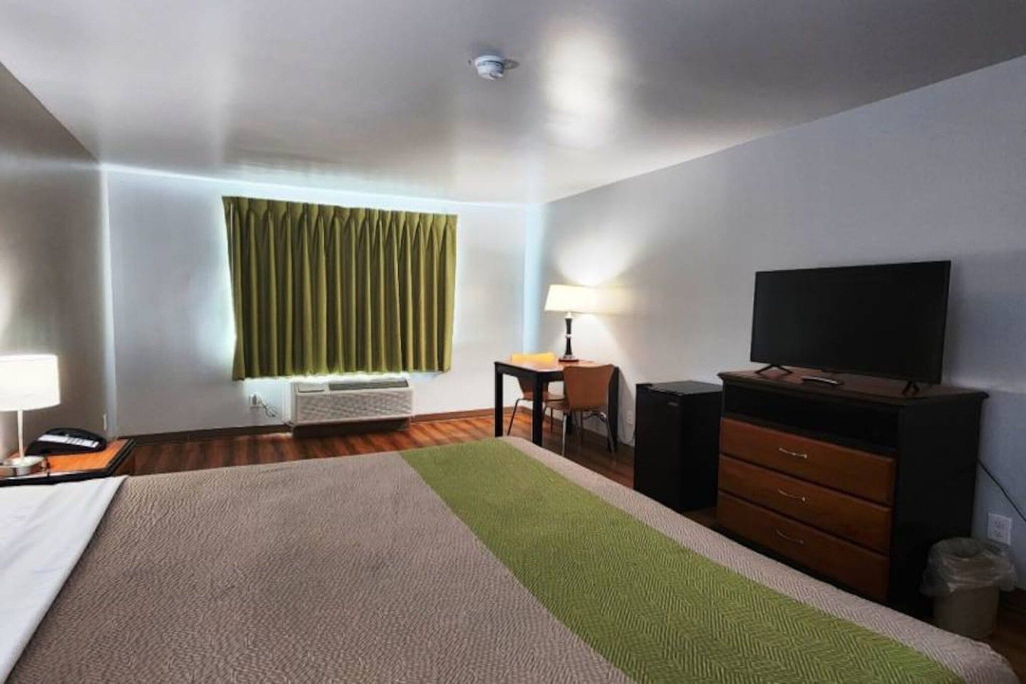 A hotel room with a bed, a desk, a chair, a television, and a window with curtains.