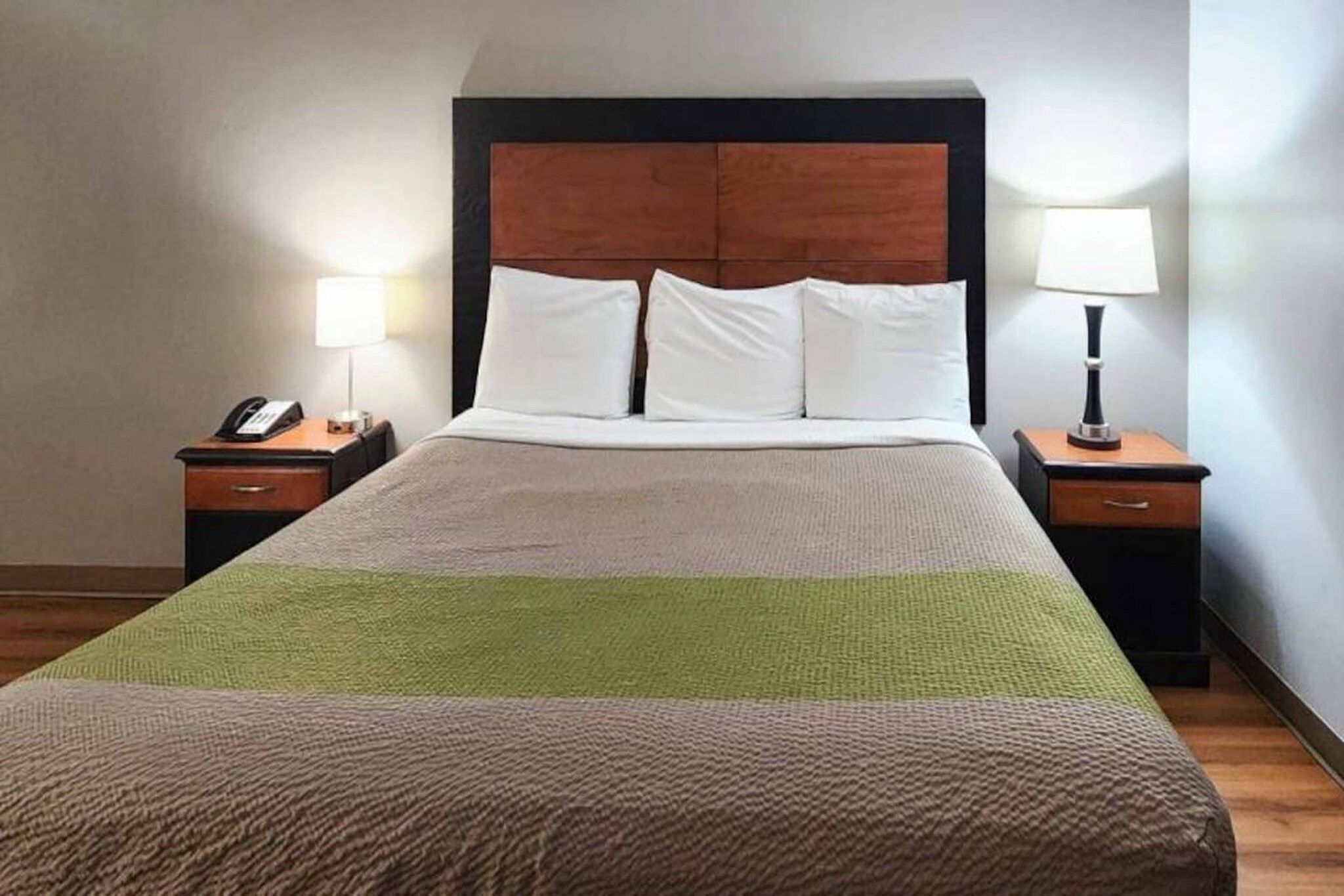 A hotel room with a large bed, two bedside tables, a wooden headboard, and two lamps.