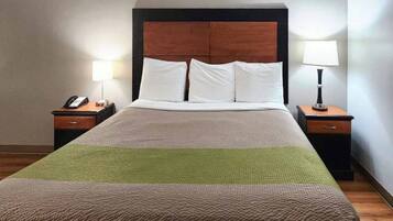 A hotel room with a large bed, two bedside tables, a wooden headboard, and two lamps.