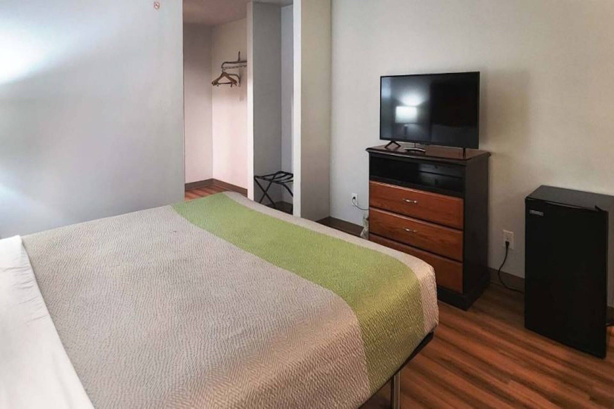 A hotel room with a bed, a television on a wooden dresser, and a small black cabinet.