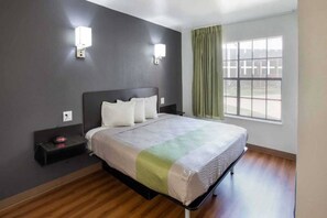A hotel room with a bed, two bedside tables, a nightstand, a window with curtains, and a view of the outside. - 1 King Bed | Non-Smoking (Arlington)
