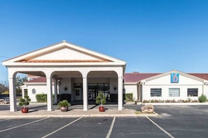 Un hôtel doté d’une entrée couverte, d’un parking et d’un bâtiment sur lequel on peut voir un panneau avec le chiffre « 6 ».