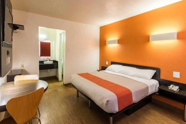 A hotel room with a bed, bedside table, chair, and a small desk with a telephone.