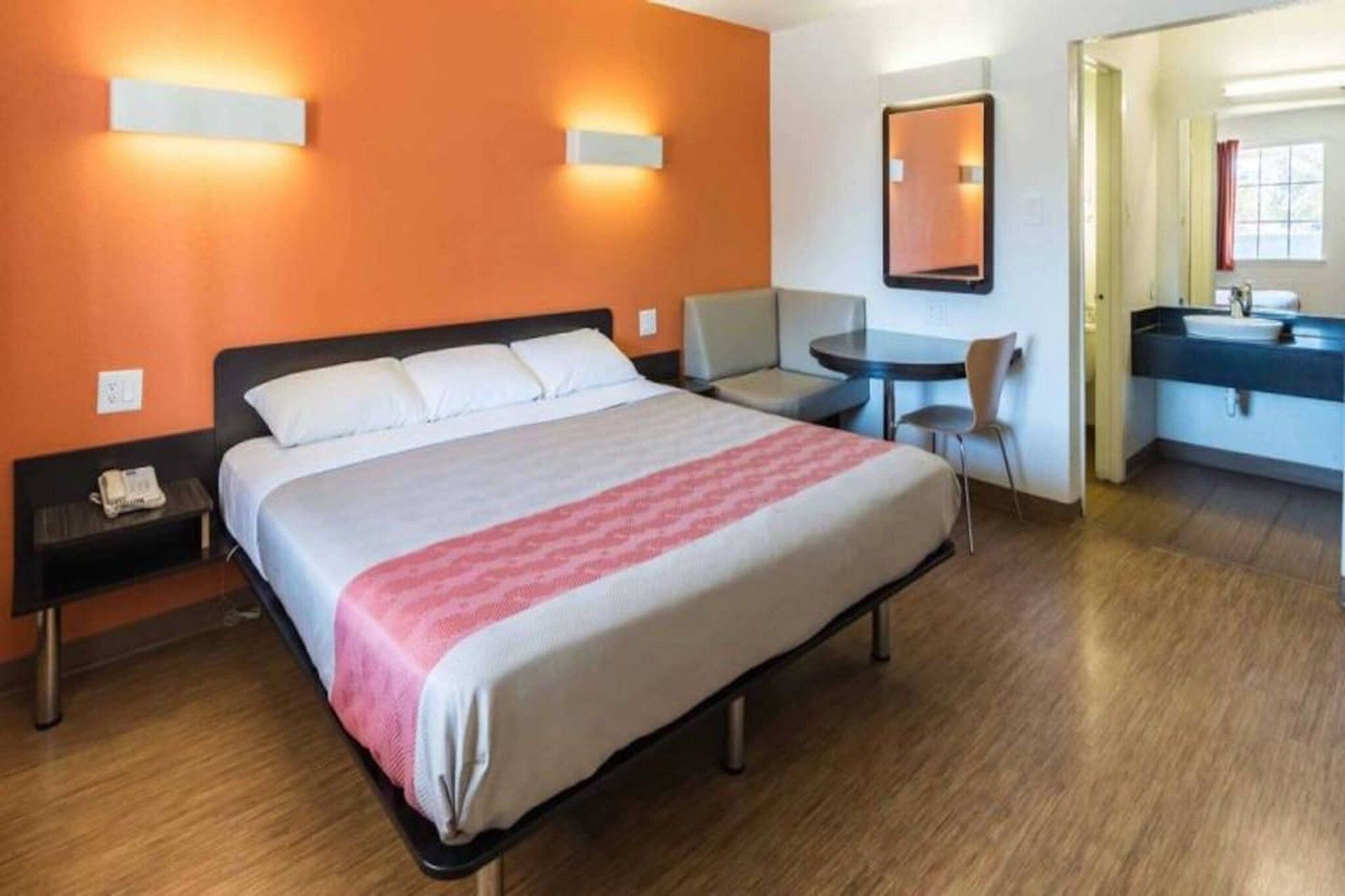 A hotel room with a bed, a desk, a chair, a mirror, and a bathroom.