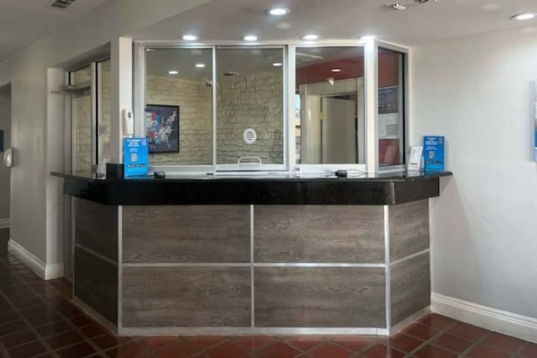 A reception desk with a glass enclosure, a stone wall in the background, and a tiled floor. - 2 Queen Beds | Non-Smoking (Dallas)