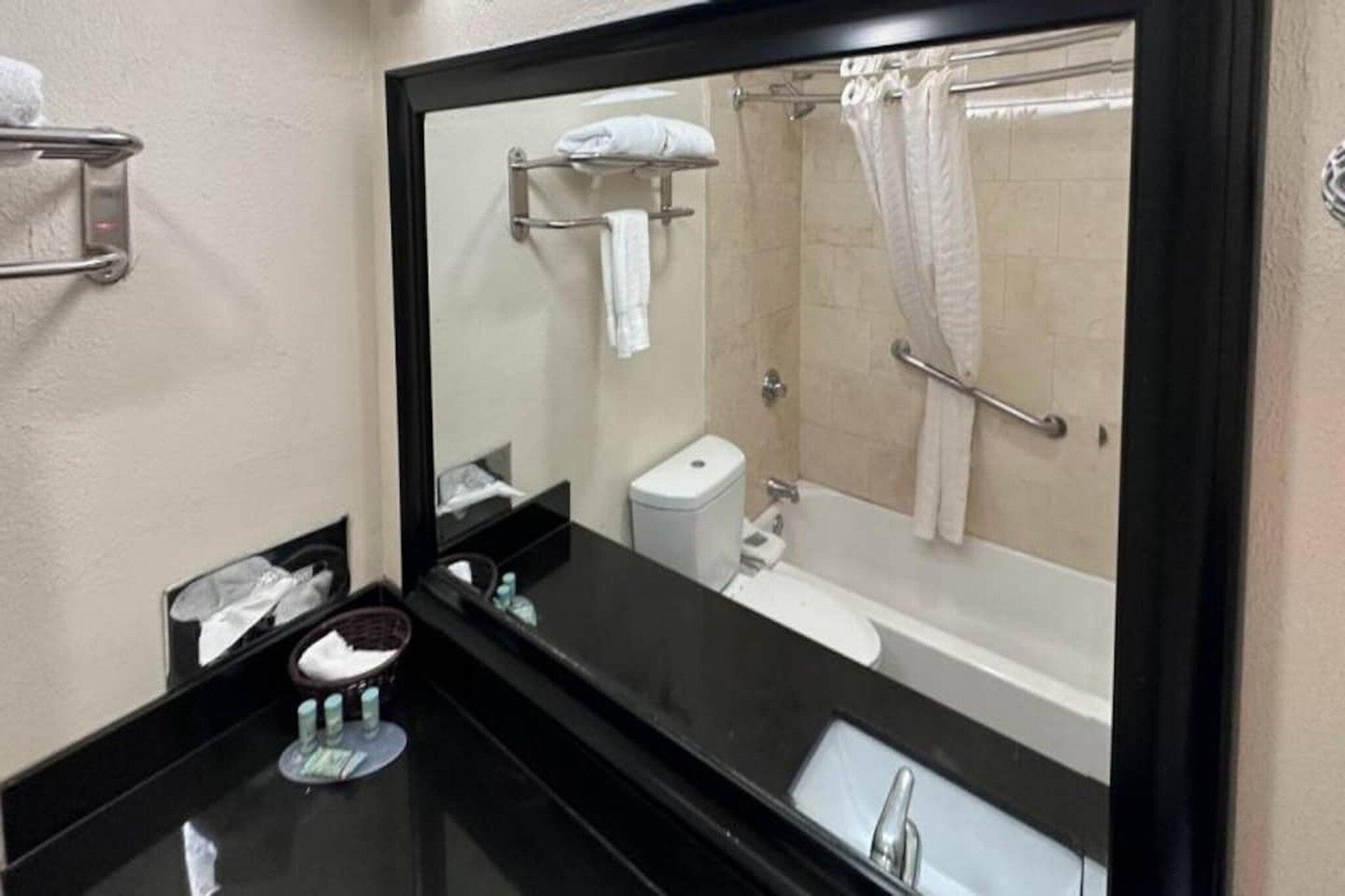 A bathroom with a black countertop, a white sink, a mirror, a toilet, and a shower with a glass door.