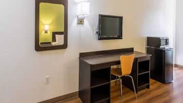 Una habitación de hotel con un escritorio de madera, una silla, un televisor, un microondas y un espejo.