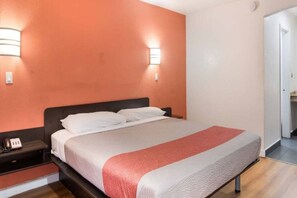 A hotel room with a bed, a bedside table, and a wall-mounted light fixture. - 1 King Bed | Non-Smoking, Micfridge (Fort Worth)