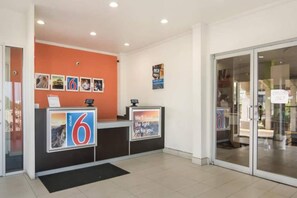 A reception area with a counter, a digital display, and a glass door leading to another room. - 1 King Bed | Non-Smoking, Micfridge (Fort Worth)