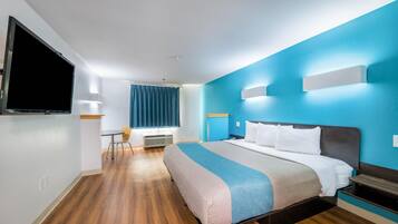 A hotel room with a bed, bedside tables, a television, a desk with a chair, and a window with curtains.