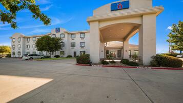 A hotel with a large entrance, multiple windows, and a parking lot.