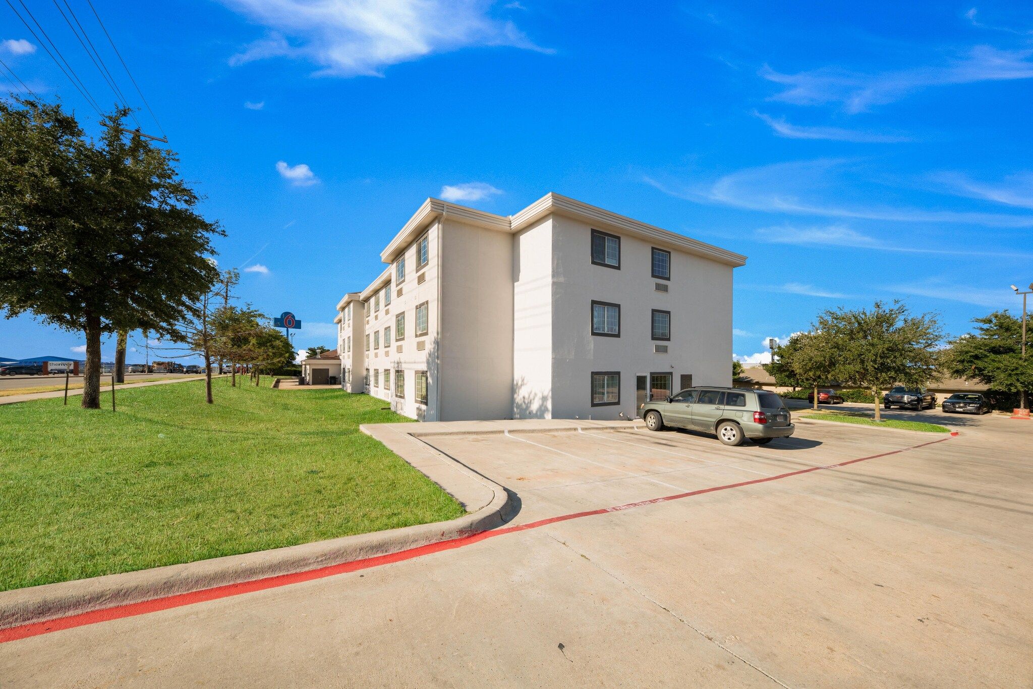 A multi-story building with a parking lot, a green lawn, and a clear blue sky.