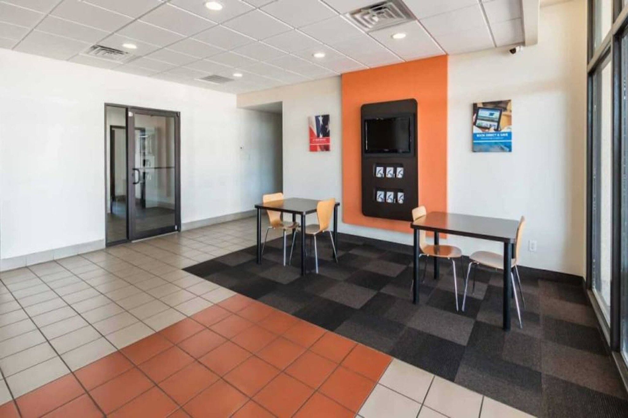 A conference room with a glass door, two tables with chairs, a blackboard, and a poster on the wall.