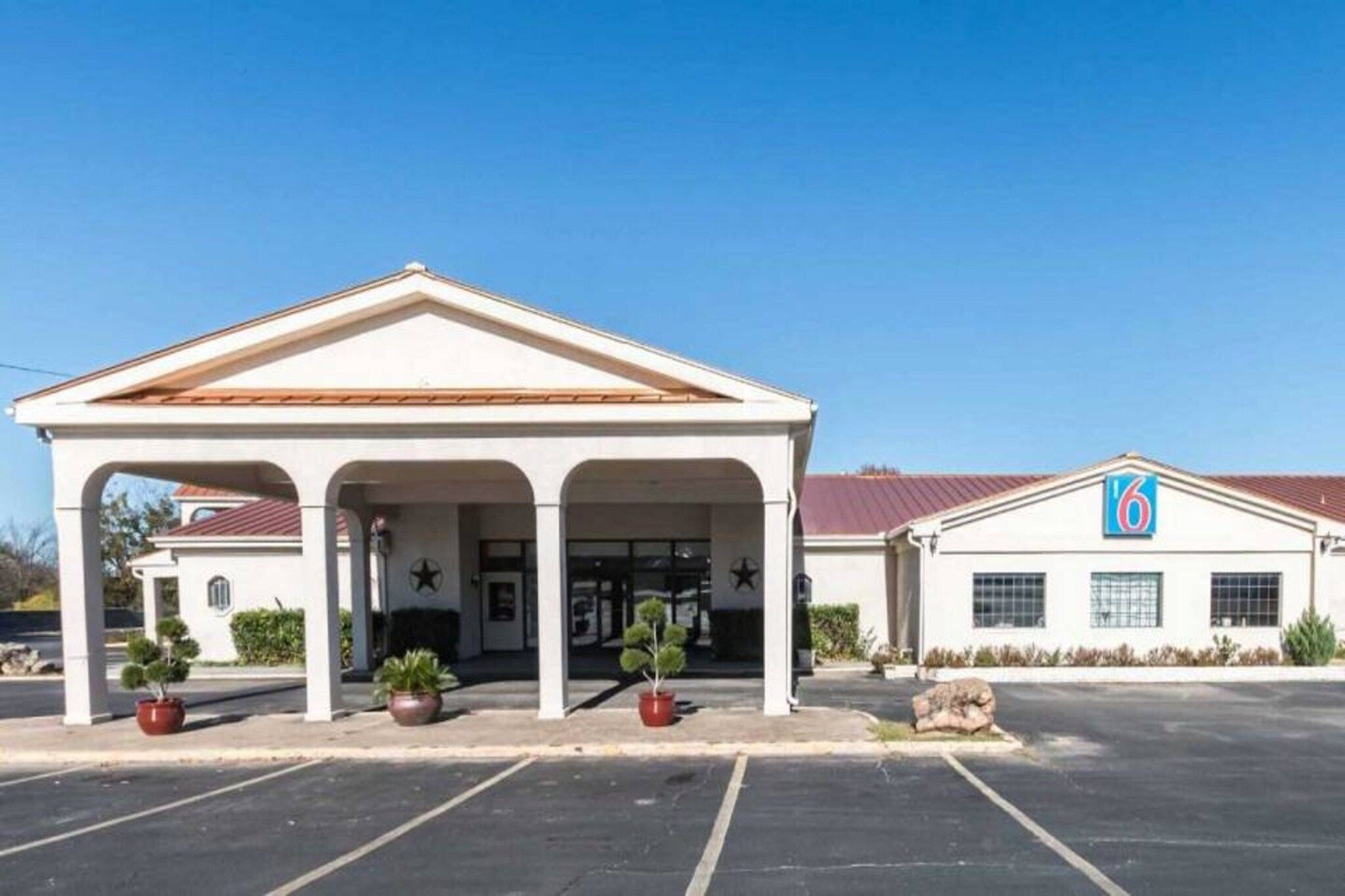 A hotel with a covered entrance, a parking lot, and a building with a '6' sign.