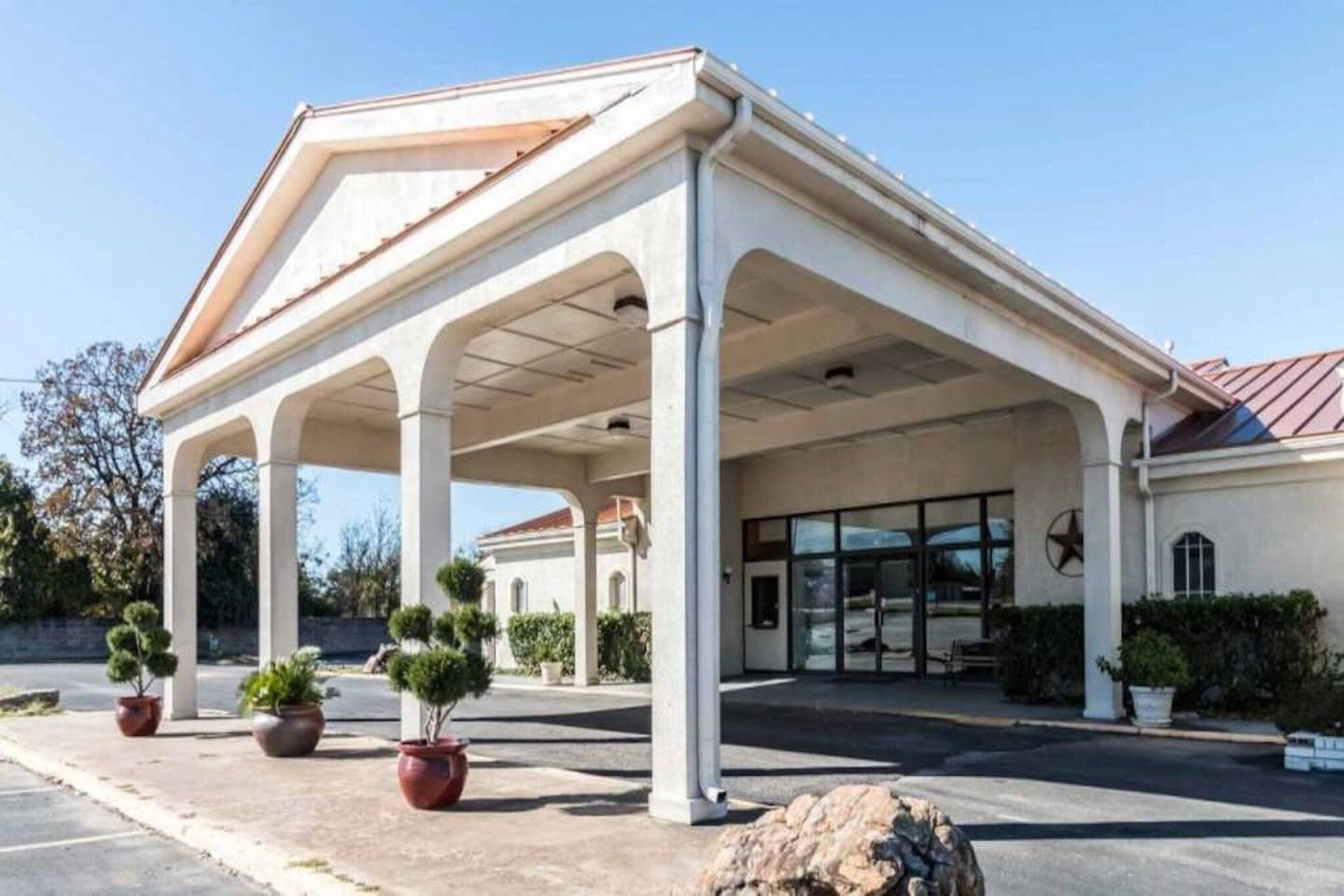 A covered outdoor area with columns, potted plants, and a building entrance.