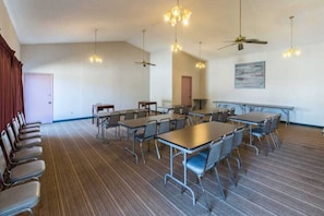 Une salle de conférence équipée de tables et de chaises, de ventilateurs de plafond et d’une porte.