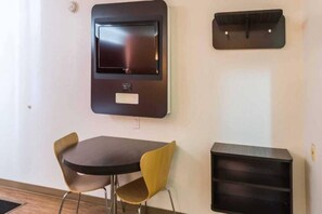 A modern room with a flat-screen TV mounted on the wall, a small table with two chairs, and a black storage unit below the TV.