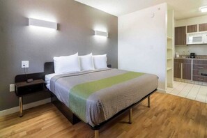 A hotel room with a bed, bedside table, and a kitchenette area. - 1 King Bed | Suite, Non-Smoking, Kitchen (Plano)