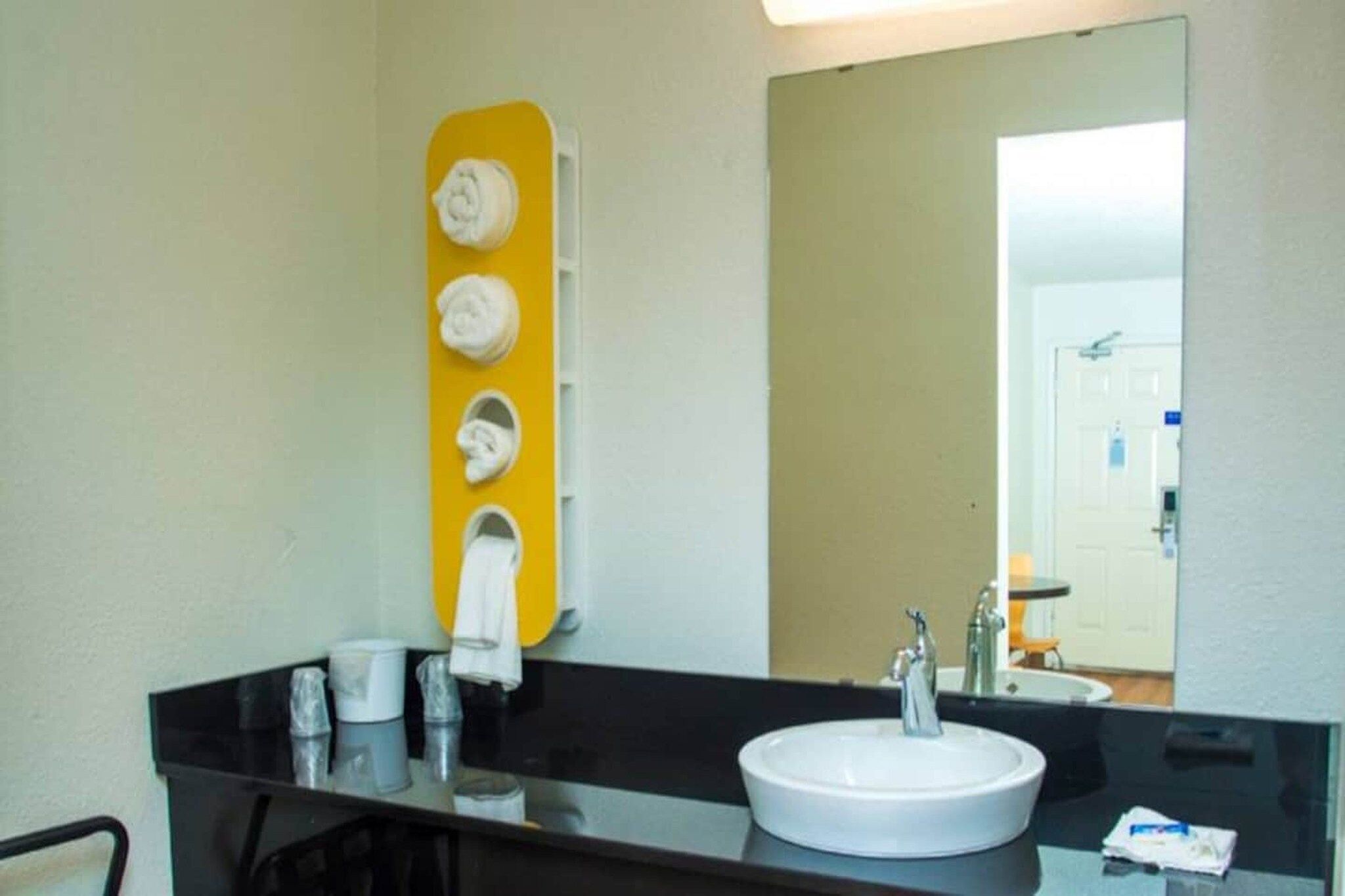 Un baño con encimera negra, lavamanos blanco y espejo.