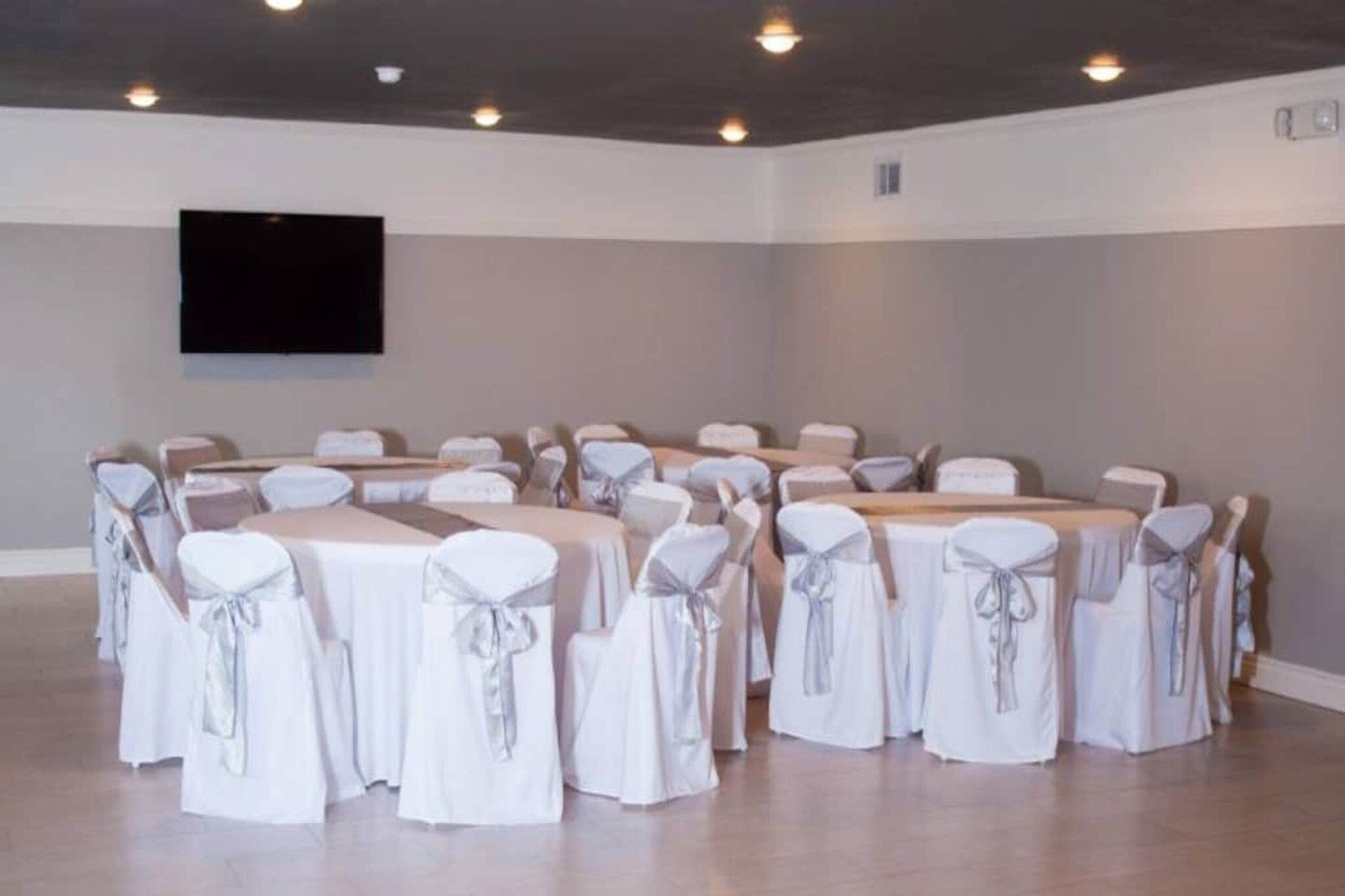 A conference room with tables and chairs, a flat-screen TV mounted on the wall, and a neutral color scheme.