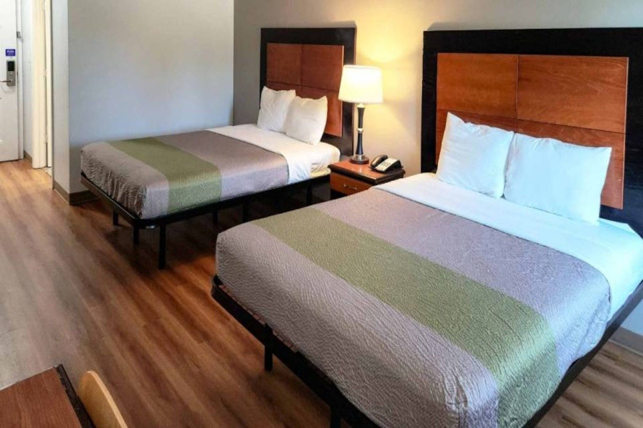 Una habitación de hotel con dos camas, una mesita de noche con lámpara y suelo de madera.
