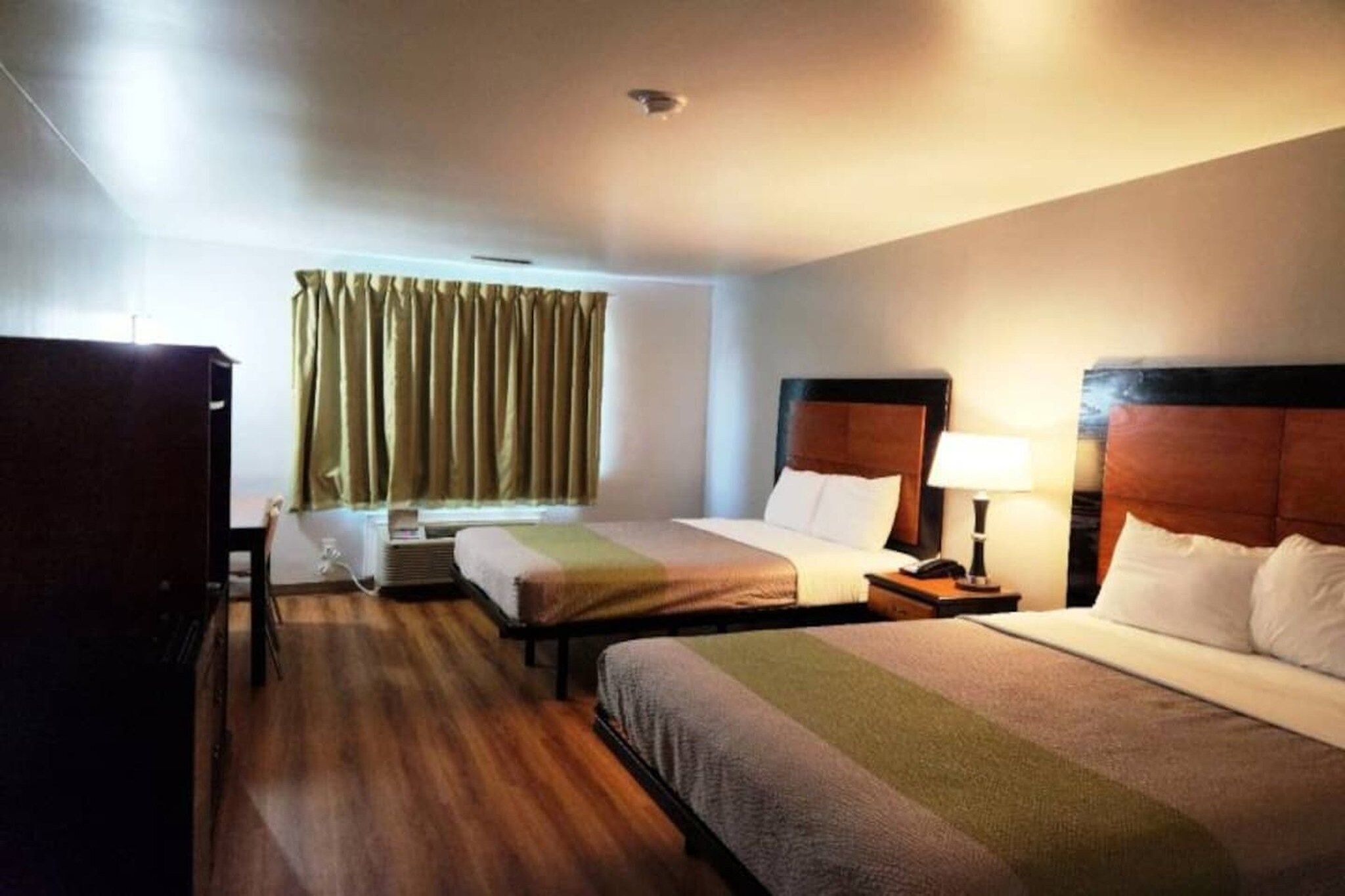 A hotel room with two beds, a desk, a chair, a window with curtains, and a ceiling light.