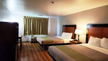 A hotel room with two beds, a desk, a chair, a window with curtains, and a ceiling light.