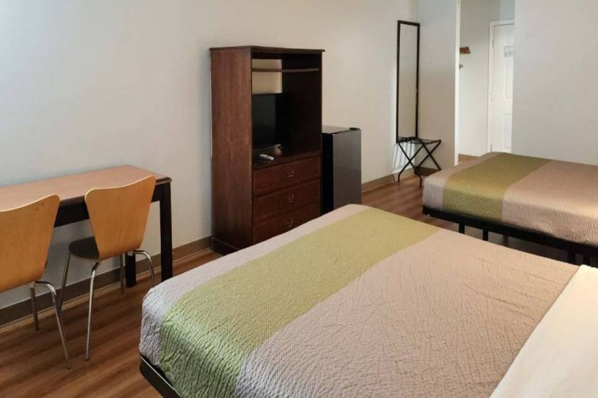A room with two beds, a desk, a chair, a wardrobe, and a mirror.