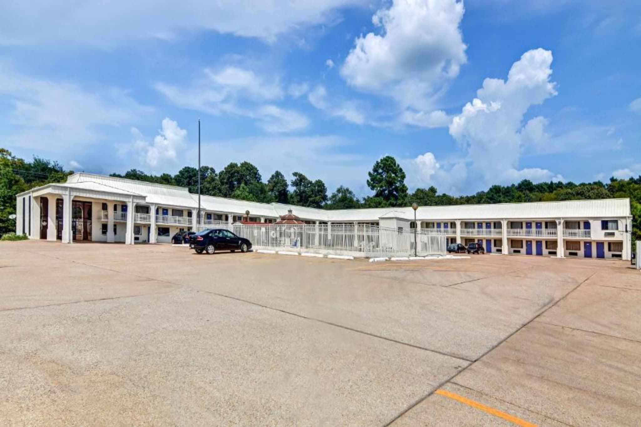A large building with a central courtyard, multiple balconies, and a parking area.