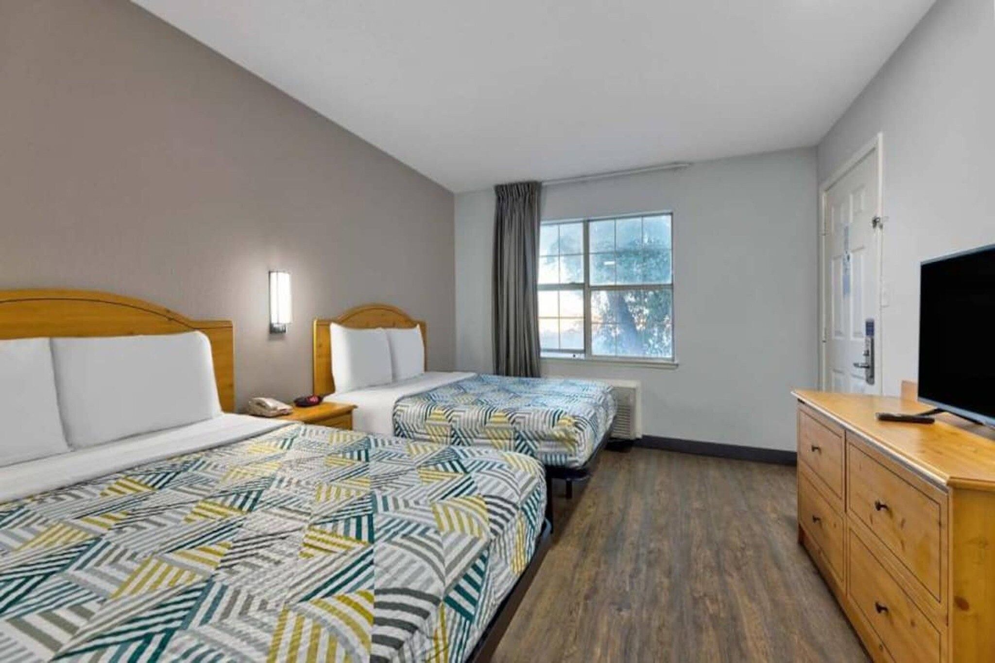 A hotel room with two beds, a TV, a dresser, and a window with a view.